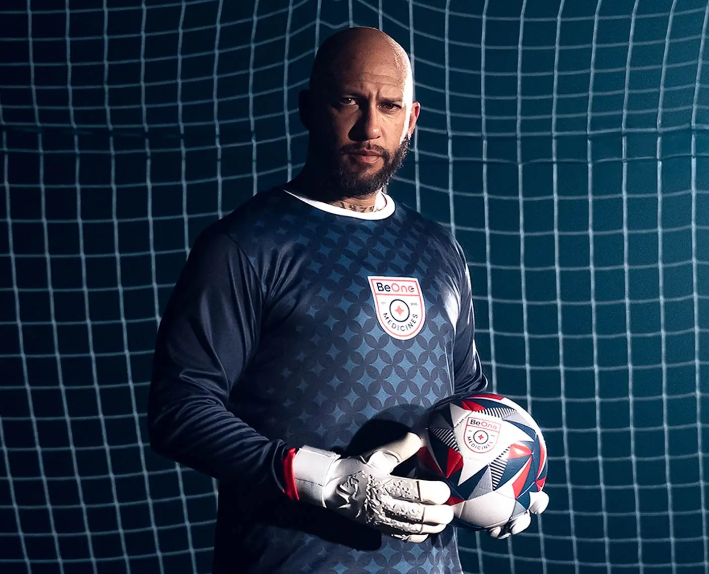Tim Howard standing with a soccer ball, representing the One Save Changes Everything cancer care campaign.